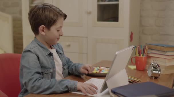 彼は彼の部屋に彼の机の上にカラフルなキャンディーを食べながら コンピュータのレッスンを受け ゲームをプレイし ビデオを見ます — ストック動画
