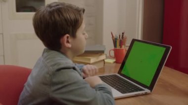 Evde bilgisayarla çalışan küçük bir okul öğrencisi yeşil ekranlı, video dinleyerek öğretmenleri dinliyor. Mesafe öğrenme. İstediğiniz resmi yeşil ekrana koyabilirsiniz.