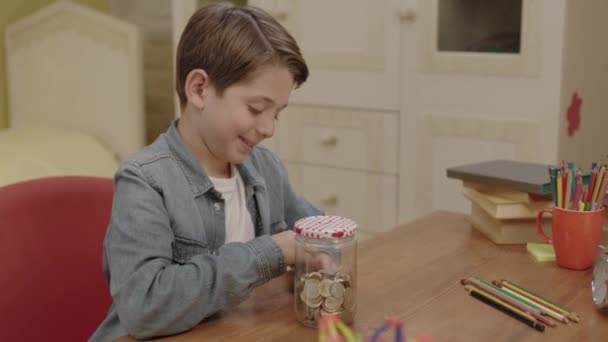 Учась Экономить Деньги Своих Родителей Мальчик Оставляет Монетку Своей Копилке — стоковое видео