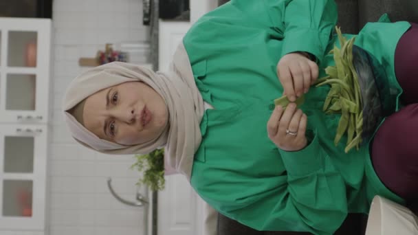 年轻女人在看电视的时候戴头巾剪绿豆 女性准备食物的肖像 垂直故事录像 — 图库视频影像