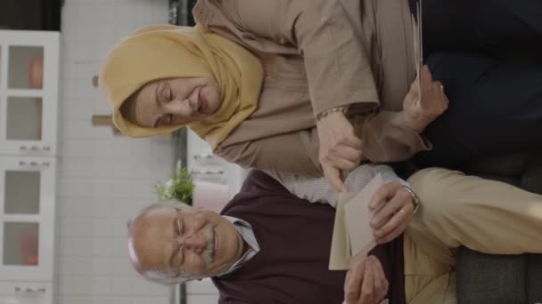 イスラム教徒のトルコ人家族は自宅のリビングルームで古い写真を見ています 彼は老人と彼のヒジャーブ妻と古い写真を見て満足しています 垂直物語のためのビデオ — ストック動画