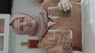 Müslüman tesettürlü kadın bir elinde kirli bir bardak, diğer elinde temiz bir bardak tutuyor. Kadın suyun kirliliğinden rahatsız oluyor ve bu soruna dikkat çekiyor..