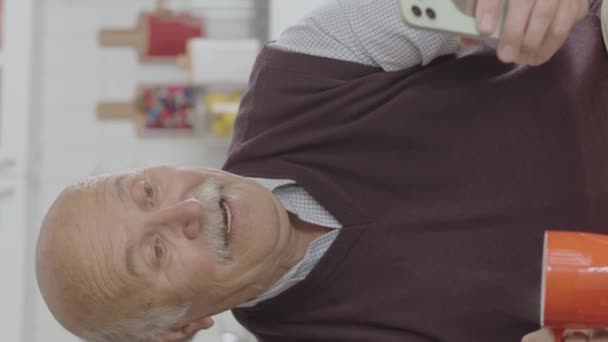 Старик Смотрит Смешное Видео Своем Смартфоне Пьет Кофе Дома Мужчина — стоковое видео
