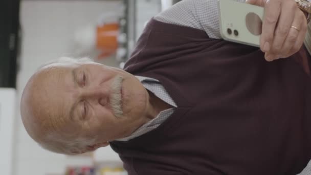 老人は電話番号をダイヤルする 老人は家にいる間に携帯電話にSmsを送る スマートフォンでモバイルアプリやSms ニュースを見ている80歳の男性 — ストック動画