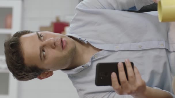 Tänksam Ung Man Som Använder Smartphone Och Dricker Kaffe Hemma — Stockvideo