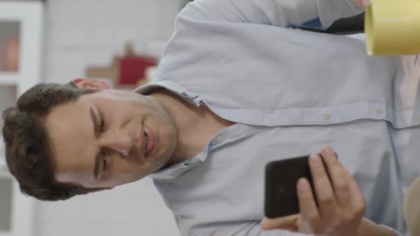 Leende Ung Man Som Använder Smartphone Och Dricker Kaffe Hemma — Stockvideo