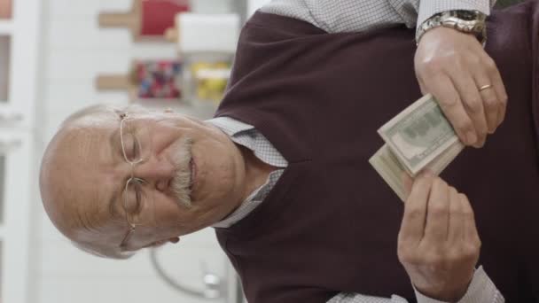 幸せな老人は非常に彼のお金に満足してオンライン宝くじを獲得した 幸せな老人は多くのドルを保持する 興奮した老人は一人で自宅で彼のドルを楽しんで 垂直話のためのビデオ — ストック動画