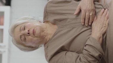 Yaşlı, beyaz saçlı, midesinde ağrı hisseden bir kadın. Yaşlılık, sağlık sorunu ve insanların konsepti. Evdeki kanepede tek başına oturan ve sindirim sisteminde sorun yaşayan yaşlı kadının videosu..