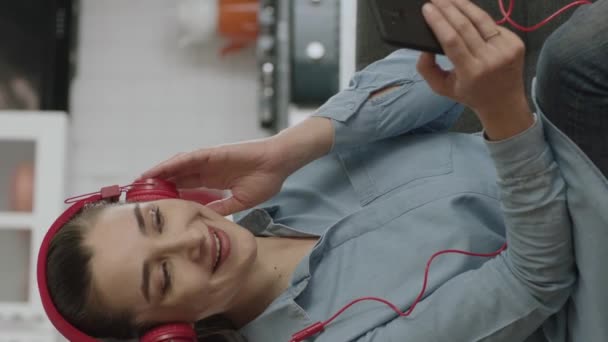 Γυναίκα Κάθεται Στον Καναπέ Χρησιμοποιώντας Ασύρματα Ακουστικά Για Ακούσετε Μουσική — Αρχείο Βίντεο