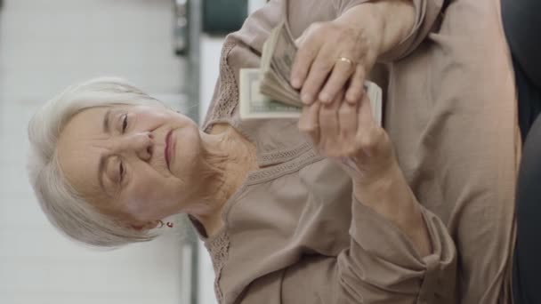 高齢女性は 銀行券を数えるリビングルームでソファに座っています ドルを計算 予算チェック お金の節約 退職金 垂直方向のためのビデオ — ストック動画
