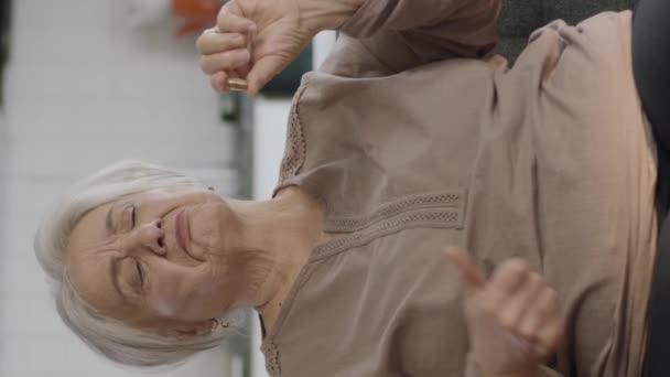 Μια Ηλικιωμένη Ασπρομάλλα Γυναίκα Δείχνει Ένα Χάπι Στο Σαλόνι Καναπές — Αρχείο Βίντεο