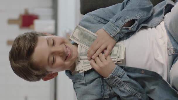 小さな男の子はソファに座って 空気中に紙幣を投げます 彼は賭けから多くのお金を稼いでいるので 幸せな人の肖像画 垂直物語のためのビデオ — ストック動画