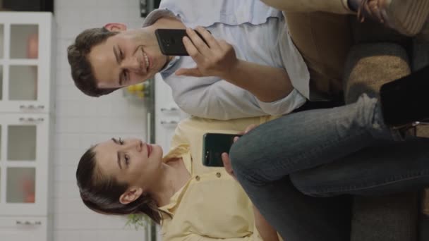 幸せなカップルは アプリを使用してスマートフォンを見てソファで笑って話しています オンラインで若いカップルのショッピング 彼らはオンラインで稼ぐお金で喜びます — ストック動画