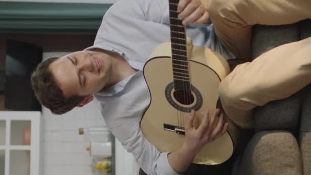 ミュージシャンがギターを弾いている 自宅で一人で時間を過ごす若い男のギタリストは ギターを演奏し 自宅で一人で彼の自由な時間を楽しむ 若者の概念 垂直物語のためのビデオ — ストック動画