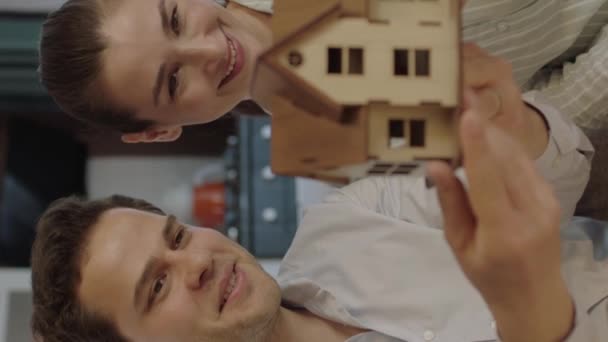 这对年轻夫妇检查了他们刚买或租的房子的模型 这对年轻夫妇看着手中的新房子的计划和模型 — 图库视频影像