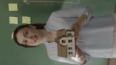 Kadın emlakçı, satış takımına ya da müşterilerine grafik tahtası önünde model evi açıklıyor. Satıcı model modeli gösterir ve insanlara evi satın almalarını tavsiye eder. Yeni inşaat projesi kavramı.