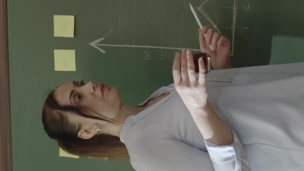 女性教師は紅茶やコーヒーを飲みながら 黒板にチョークで書かれたメモや数式で数学を説明します 彼女は学生の将来の生活の成功を助けるために最善を尽くしています — ストック動画