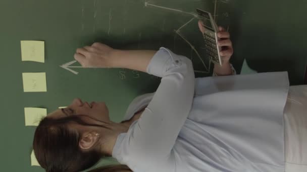 黒板の前の生徒にチョークノートや数式で数学を説明する女性教師 彼女は彼女の学生が彼らの将来の生活の中で成功を助けるために最善をしようとします — ストック動画