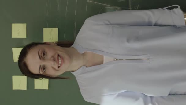 여교사는 종이와 분필된 공식을 가지고 카메라로 웃으며 공간을 바라본다 온라인 — 비디오