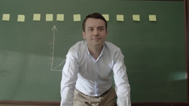 黒板の前に立つ男性教師は メモやチョークで数式を描き カメラで笑顔で学生たちに教えていました オンライン距離教育 — ストック動画