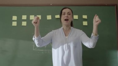 Female teacher standing in front of blackboard with glued notes and chalked math formulas, smiling at camera and happy that her students are succeeding. Successful school or teacher concept.1