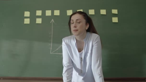 女教师站在黑板前 手里拿着粘贴的笔记和粉笔画着数学公式 对着相机微笑 给她的学生授课 网上远距离教育 — 图库视频影像