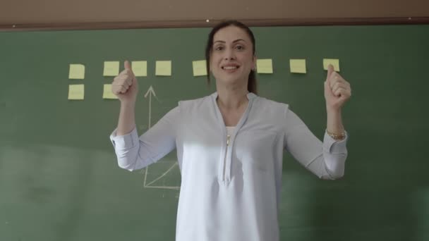 女教师站在黑板前 带着粘贴的笔记和粉笔画的数学公式 对着摄像机笑着 对她的学生的成功感到高兴 成功的学校或教师概念 — 图库视频影像