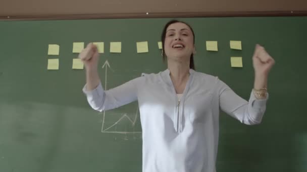 女教师站在黑板前 带着粘贴的笔记和粉笔画的数学公式 对着摄像机笑着 对她的学生的成功感到高兴 成功的学校或教师概念 — 图库视频影像