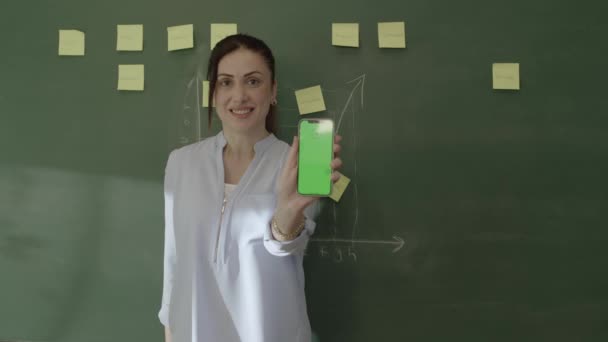 课堂上的年轻女教师在智能手机上浏览社交媒体账户 浏览网页 阅读电子邮件 对自己看到的一切感到惊讶 并向摄像机展示自己的绿色屏幕手机 — 图库视频影像