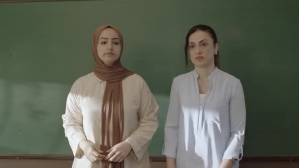 Female Teacher Hijab Female Colleague Looking Camera Front Blackboard Classroom — Stockvideo