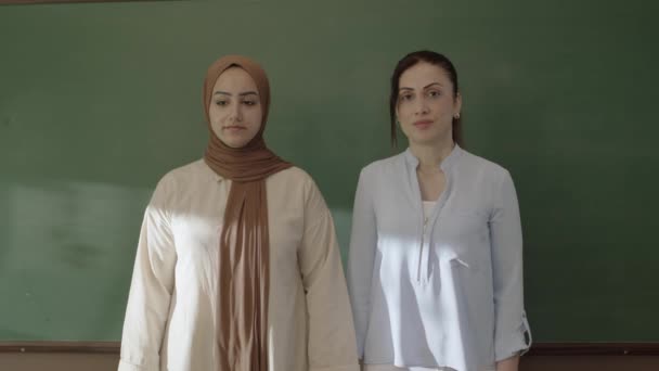 Female Teacher Hijab Female Colleague Looking Camera Front Blackboard Classroom — Stockvideo