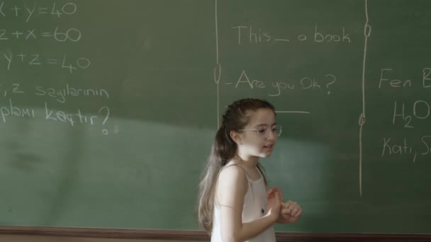 緑の黒板の前で彼女の試験のために勉強していない神経女子学生の文字の肖像画 教室の黒板の前を左に歩いています — ストック動画