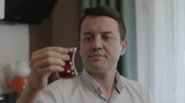 Meaningful tea experience of herbal or green tea(turkish tea) by a young man. Portrait of a man satisfied with the color and smell of tea in the kitchen. Turkish breakfast concept.