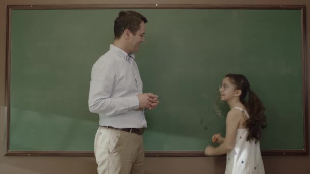 学校のコンセプトに戻る 若い男性の先生は教室で学生を抱きかかえた 幸せな女の子は彼女の先生を見て非常に満足しています — ストック動画