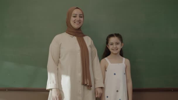 Happy Hijab Dressed Female Teacher Little Schoolgirl Classroom Arms Folded — Vídeo de Stock