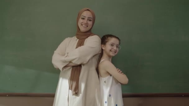 Happy Hijab Dressed Female Teacher Little Schoolgirl Classroom Arms Folded — Stockvideo