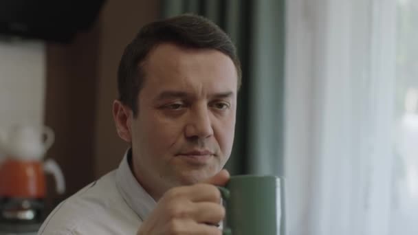 自宅から離れた職場でコーヒーを飲みながら カメラで微笑むビジネスマン 男飲みコーヒーのクローズアップポートレート — ストック動画