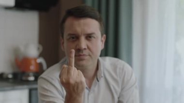 Young man showing middle finger, angry and disobedient at bad behavior. In the kitchen, the middle finger points badly at the camera and asks not to be disturbed.Close-up video.