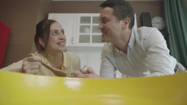 View of people cooking from a pot or pan. They are tasting the food in the cooking process with a wooden spoon in the kitchen. The camera is inside the pot.