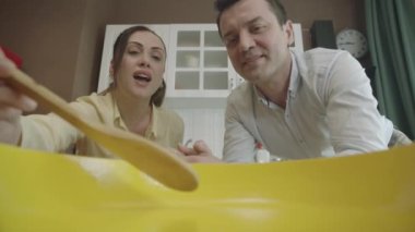 View of people cooking from a pot or pan. They are tasting the food in the cooking process with a wooden spoon in the kitchen. The camera is inside the pot.