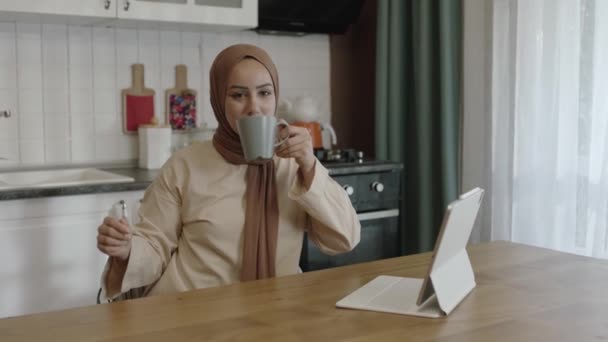 Young Woman Hijab Works Remotely Tablet Computer Woman Drinks Coffee — Stockvideo