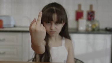 Little girl angry, angry and disobedient at bad behavior showing middle finger. In the kitchen, the middle finger points badly and asks not to be disturbed. Provocation and rude attitude.