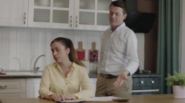 Young married couple checking payment bills in kitchen at home. They manage the family budget, discuss spending money, have problems with payments. They calculate double bills, they experience stress.