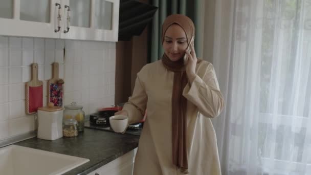 Молодая Мусульманка Хиджабе Готовит Еду Кухне Одновременно Разговаривает Мобильному Телефону — стоковое видео