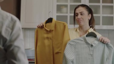 Unable to decide which outfit to wear, the young woman asks his wife to choose the outfit to wear. The woman holding two shirts cannot decide which shirt to wear. Inability to choose clothes.