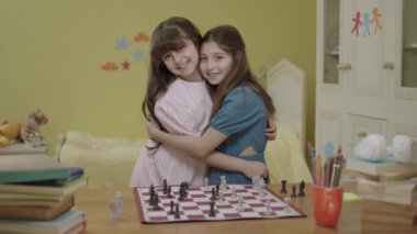 Portrait of smart little girls playing chess in their room, loving each other, smiling at camera. The development of logical thinking in children. Mind and intelligence. To develop logical thinking.