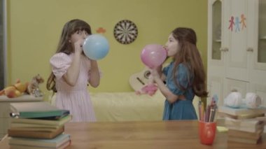 Little girls are blowing air into the balloon. Happy birthday party, celebration. Children are having fun by inflating balloons in their rooms. Cute kids inflate the balloon for their birthday.