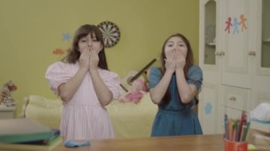 Little girls are having fun together by dancing in their room at home. Happy girls are having a crazy party at their house. Funny kids dancing, jumping, singing are sending air kisses to the camera.