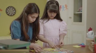 Two beautiful sisters or friends doing puzzles at home. Children teach each other how to solve puzzles. Two little girls sitting together at the table solving puzzles. Intelligence games.