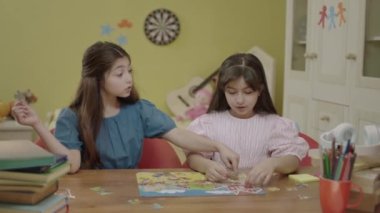 Two beautiful sisters or friends doing puzzles at home. Children teach each other how to solve puzzles. Two little girls sitting together at the table solving puzzles. Intelligence games.